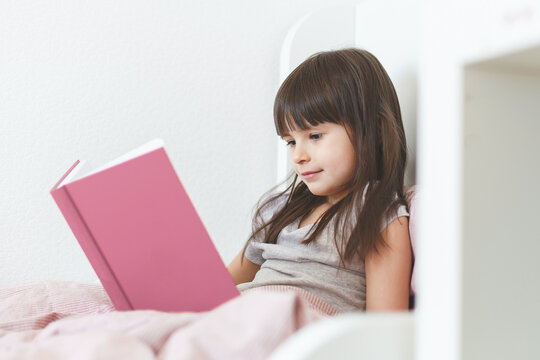 one todder girl 5 years old brunette with long hair sits in bed and reads a book
