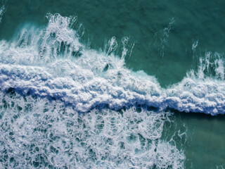 Aerial landscape looking down at crushing turquoise ocean waves. Top down aerial view of sea water surface. White foam waves texture as natural background.