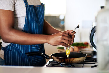 Fried eggs are his favourite. Cropped shot of an unrecognizable man frying eggs while making breakfast in his kitchen at home.