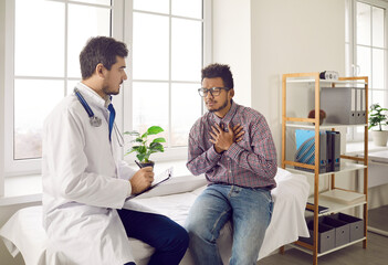 Obraz premium Unhealthy ethnic man suffer from heartache or heart attack have consultation with cardiologist in private hospital. Sick young biracial guy struggle with pain chest consult with doctor in clinic.