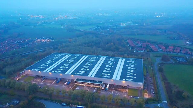 Aerial shot orbital around a warehouse at night (dusk), circled by vegetation. Wattrelos, France