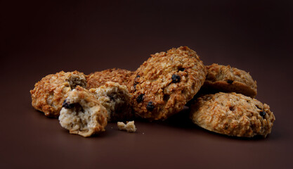 Whole and crushed handmade oatmeal cookies on a brown background.