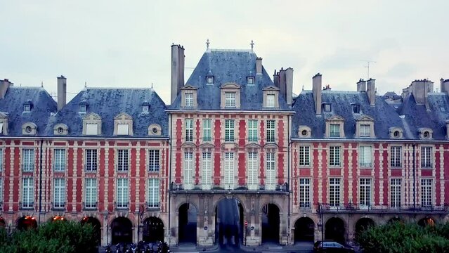 Ascending drone view of Pavillon de la Reine, historic house with arcades at Place des Vosges, Paris, France. Revealing city panorama.