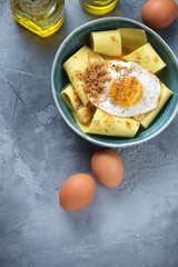Bowl of parmesan broth with rag pasta and crispy fried egg, flat lay on a grey concrete background, vertical shot with space