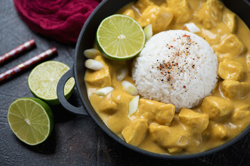 Close-up of yellow curry with chicken and white rice in a cast-iron pan, selective focus