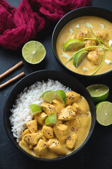 Black bowls with yellow chicken curry and white rice, studio shot on a black stone background, selective focus