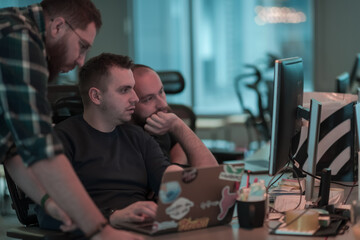 A photo of three men staring intently at a computer while sitting in a modern office. Selective focus 