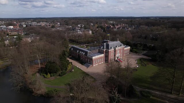 Sideways aerial pan  showing Slot Zeist castle with the moated manor surrounded by green park and urban landscape in the background. Dutch stately venue seen from above.