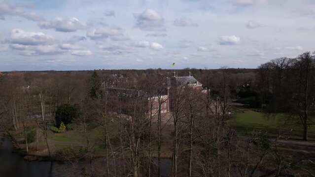 Winter barren branches and trees revealing aerial of Slot Zeist castle with the moated manor surrounded by green park and urban landscape in the background. Dutch stately venue seen from above.