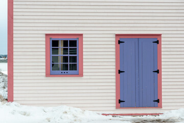 The exterior wall of a white wooden cape cod clapboard siding house with a purple panel door and...