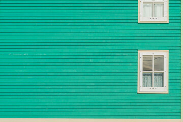 A traditional wooden clapboard exterior wall of a vibrant teal green house with two single hung...