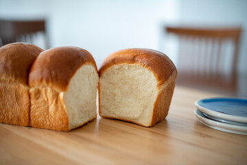 A single loaf of fresh white bread on a wooden cutting board in a kitchen. The warm crisp bun has...