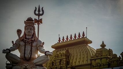 Shiva statue near Hindu temple with a bright golden roof, India