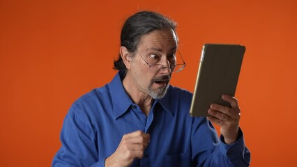 Annoyed shocked businessman in eyeglasses using tablet while browsing internet. Irritated man monitoring statistics on modern device. Trouble concept