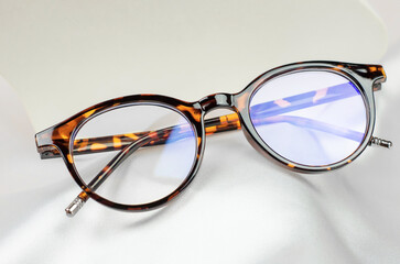 Leopard-colored glasses on a white silk fabric, close-up