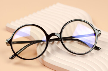 Stylish round glasses for vision on a wavy beige podium