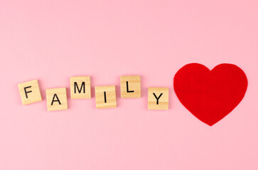 The word family from wooden letters and a red heart on a pink background