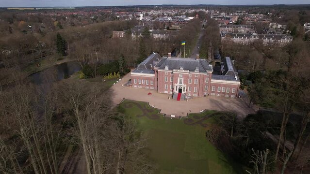 Sideways aerial movement showing slot Zeist castle with the moated manor surrounded by green park and urban landscape in the background. Dutch stately venue seen from above.