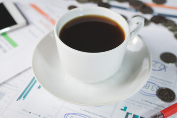 A cup of black coffee on an investor's desk with a financial report