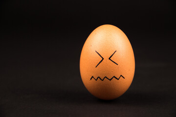 Closeup of an outline smiley face drawing on a brown egg on a dark surface