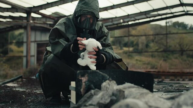 Man wearing a gas mask finds a stuffed animal in a war-torn hospital