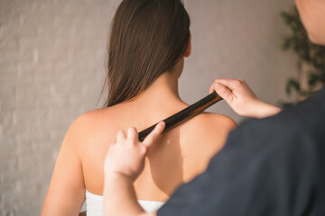 Close-up of a young woman undergoing reflexology. a masseur massages a young girl's back with a bamboo stick in a spa salon. the concept of body skin care