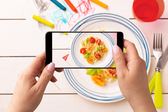 Woman taking photo of kid’s dinner (spaghetti) with smartphone. Posting food photos on social media.