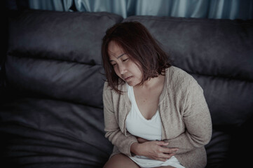 Asian sick woman sit on the sofa stay at home,The woman felt bad, wanted to lie down and rest,stomach ache,menstrual pain