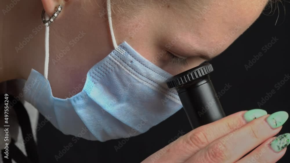 Poster girl scientist looks into the lens of a microscope in a mask close-up. the study of the structure of