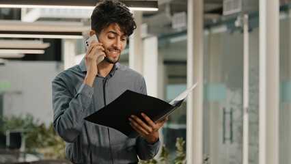 Busy arab man businessman worker in office workspace talking mobile phone answer call consulting clients discussing financial issues holds folder documents statistical data negotiating project profit