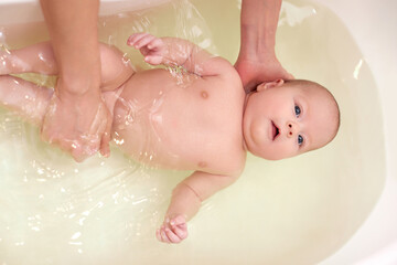 Fototapeta premium mother bathes her baby in a white small plastic tub