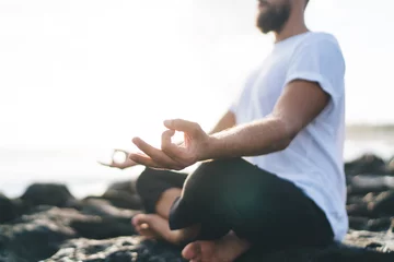 Fotobehang Concentrated male yogi dressed in comfortable wear meditating in lotus pose enjoying relaxation and concentration time at seashore rock, concept of holistic recovery and mental healthy lifestyle © BullRun