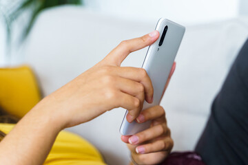 Unrecognizable young woman using a phone while lying on a sofa
