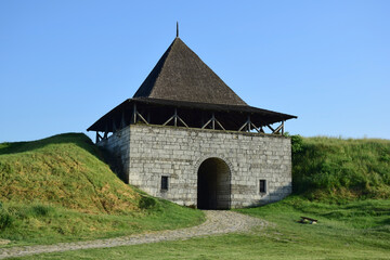 Fototapeta na wymiar Large tower of a medieval stone fortress with an arched entrance and earthen ramparts on the sides