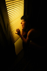 Vertical shot of a mystery Caucasian woman screaming through blinds in a dark room