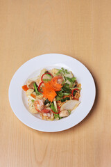 Stir fried noodles with seafood are placed on a white plate, on a wooden table
