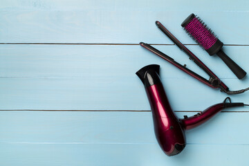 Hair dryer, straightener and brush on wooden background, top view