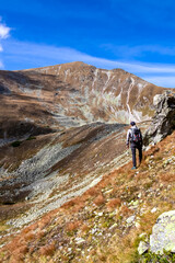 Obraz premium Man with backpack with view on Haemerkogel in the Lower Tauern mountain range, Styria, Austria, Europe. Sunny autumn day in Seckau Alps. Scenic hiking trail to Seckauer Zinken on dry, bare terrain.
