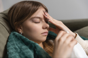 Fototapeta premium Sick girl lies on the couch covered with a blanket and holds a paper napkin in her hand