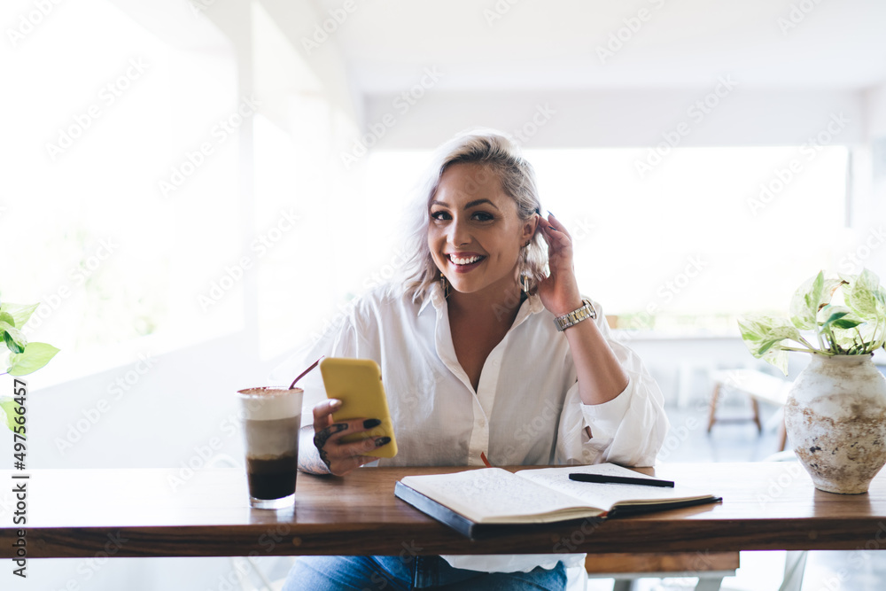 Poster portrait of happy female blogger with modern smartphone device and textbook smiling at camera enjoyi