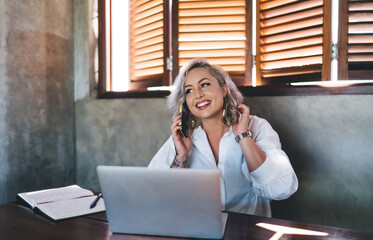 Cheerful female copywriter smiling while discussing creative ideas using cellphone application in...