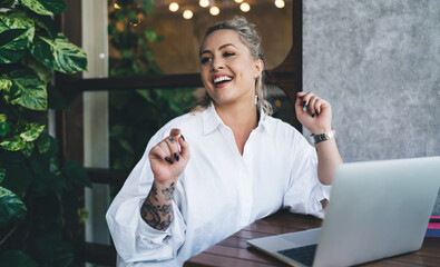 Happy IT professional with laptop computer working remotely at coworking terrace, successful female freelancer with netbook technology looking away and smiling during daytime for doing distance job