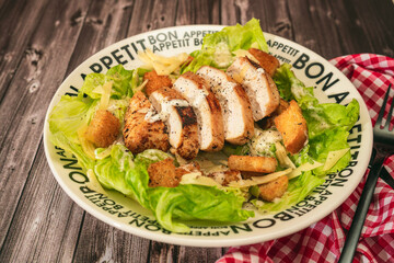 Caesar salad with thinly sliced chicken breast and traditional aioli on a plate that says bon...