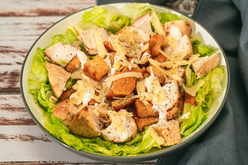 Exquisite Caesar salad with small bites of chicken and a traditional aioli sauce in a small bowl on a rustic table. High view.