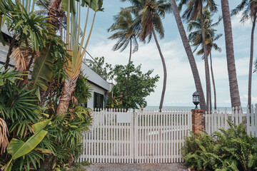 Fototapeta na wymiar Tropical garden with wooden white fence on backyard at coastline