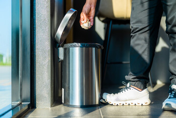 Closeup foot and sneaker of a woman place on the tread of step-open trash can in the room to drop...