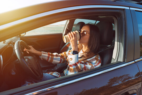 Young beautiful stylish woman driving her new car and drinking coffee on a sunny day. Concept for car rental