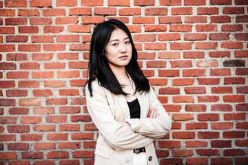 confident beautiful chinese business woman with arms crossed standing over bricks wall background