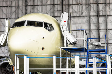 Cockpit and nose of the aircraft close up in a hangar on the service, with open doors.