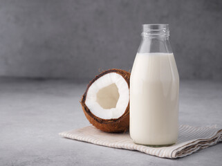 Coconut vegan milk is non dairy products in a bottle with a place to copy on a gray concrete background. Glass bottle of milk or yogurt with coconut chips aside. Concept of healthy eating. Close up.